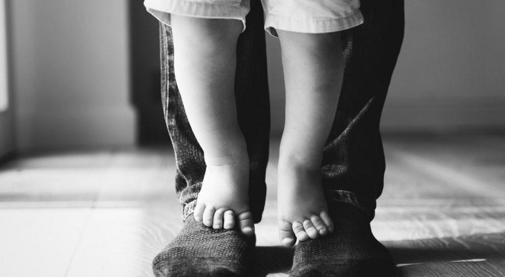 Baby feet standing on top of adult feet