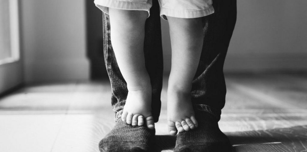 Baby feet standing on top of adult feet