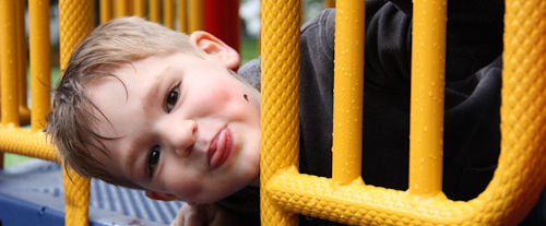 young boy playing on a playground set sticking his tongue out