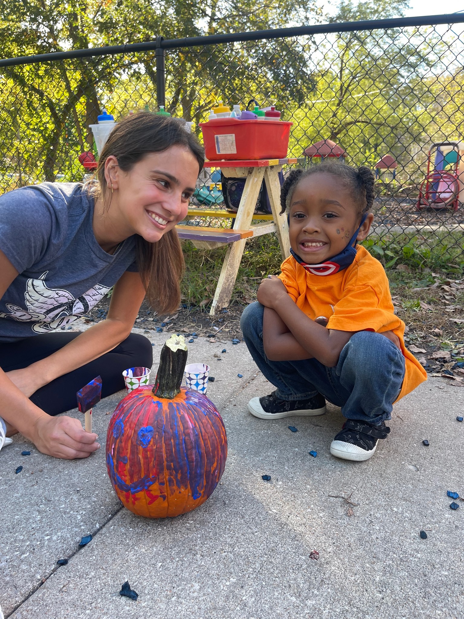 teacher and her student sitting on sidewalk and painting a pumpkin