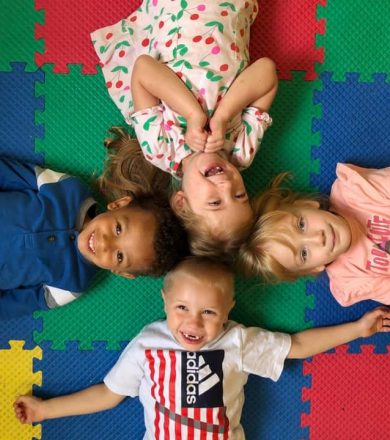 4 young children laying on a multi colored floor smiling at the camera