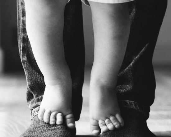 black and white photo of a a child's feet standing on top of a grown person's socked feet
