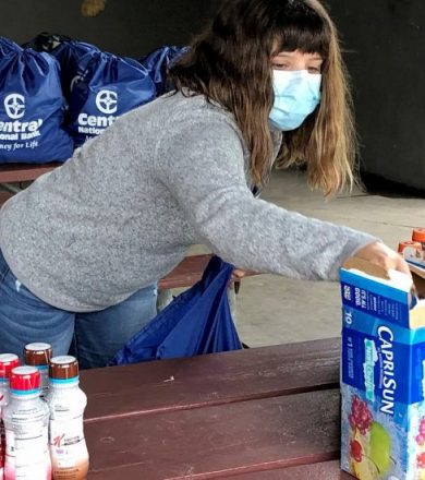 A woman wearing jeans, a grey sweater and a face mask puts together care packages
