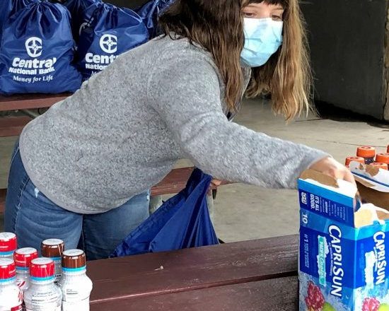 A woman wearing jeans, a grey sweater and a face mask puts together care packages