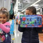 Two young children inside a Wal-Mart. Each are holding up a toy they selected.