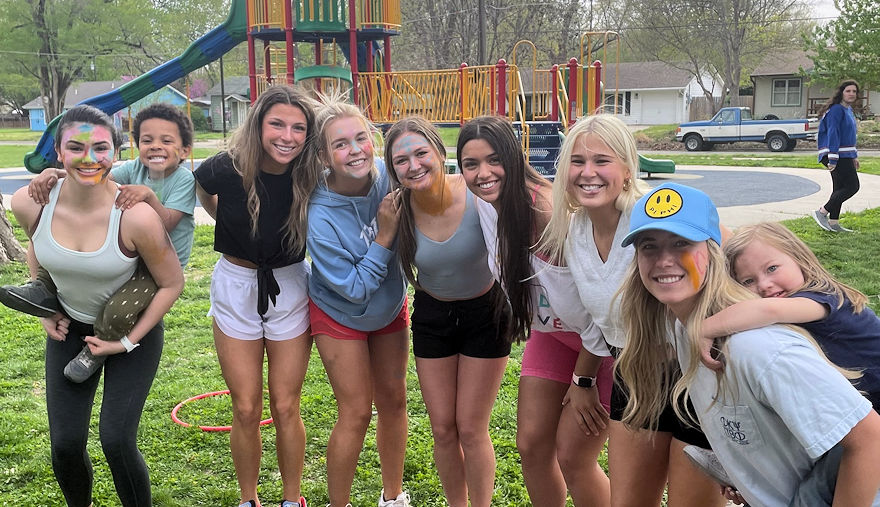 a group of teenage girls standing together at a playground and two have young children on their backs