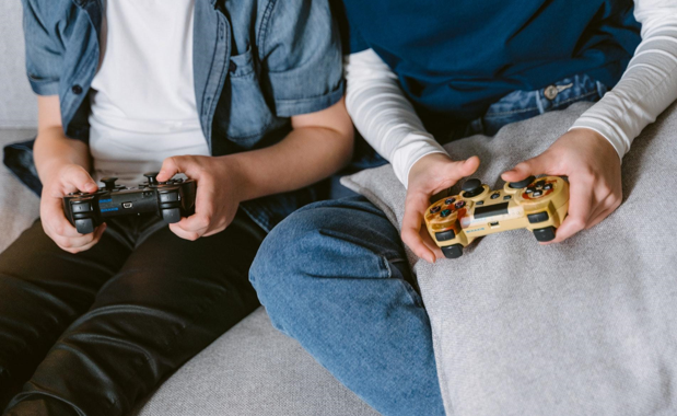 two people sitting on couch holding game consoles