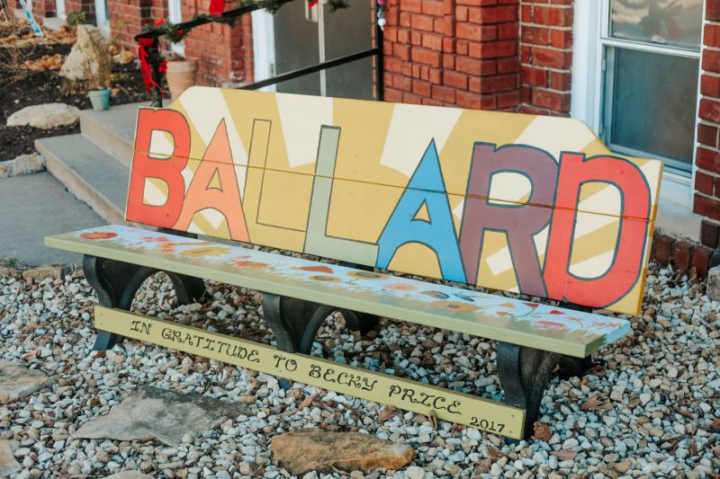 park bench with the word Ballard painted on the back in multi colored letters