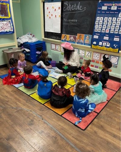 teacher with her students in a classroom. they are all sitting down in a circle and learning