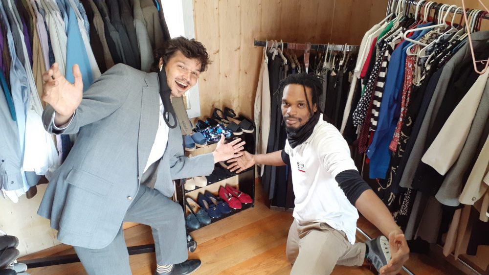 two men with their arms spread out in front of racks of shoes and clothes